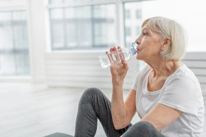 Persona mayor bebiendo agua mientras está sentada en el suelo con ropa deportiva
